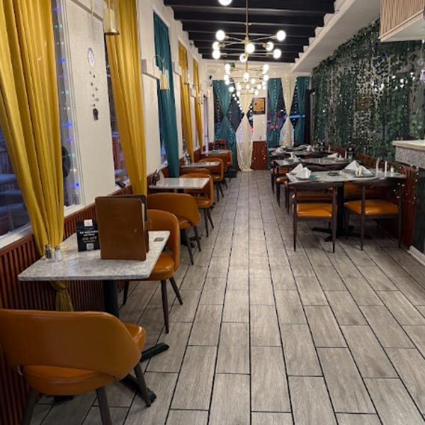 Elegant restaurant dining room with mustard curtains, teal accents, set tables, pendant lighting, and tiled floors.