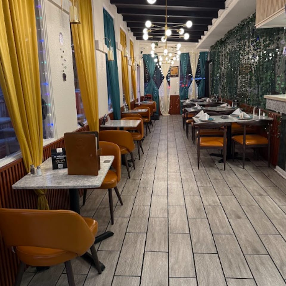 Elegant restaurant dining room with mustard curtains, teal accents, set tables, pendant lighting, and tiled floors.